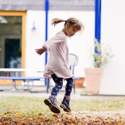 Kita-Kind springt durch Laub.